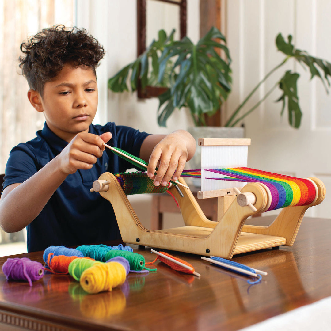 Instruktorka pokazuje dziewczynce jak przesuwać suwak na krośnie tkackim